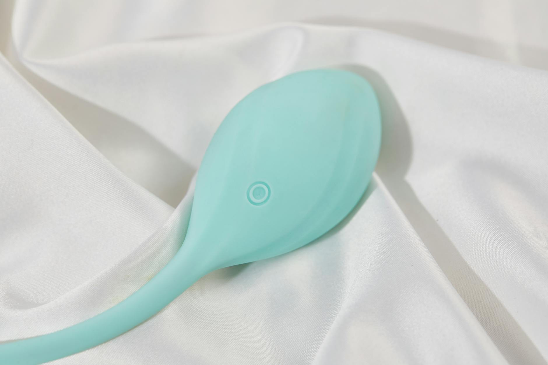 A sleek teal vibrator resting on white silk fabric, symbolizing sensual self-care and personal pleasure.