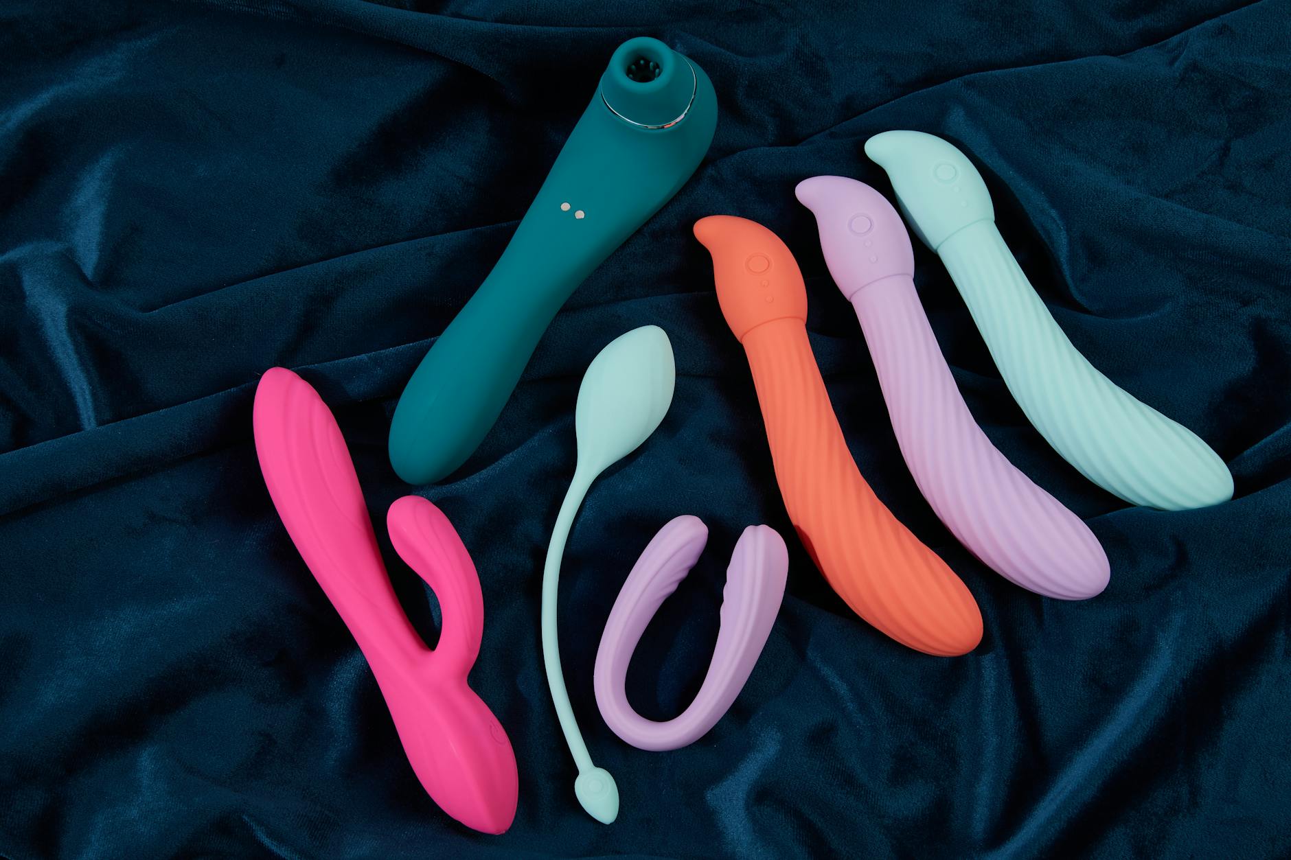 Colorful silicone vibrators displayed on dark blue fabric, showing variety of shapes and textures