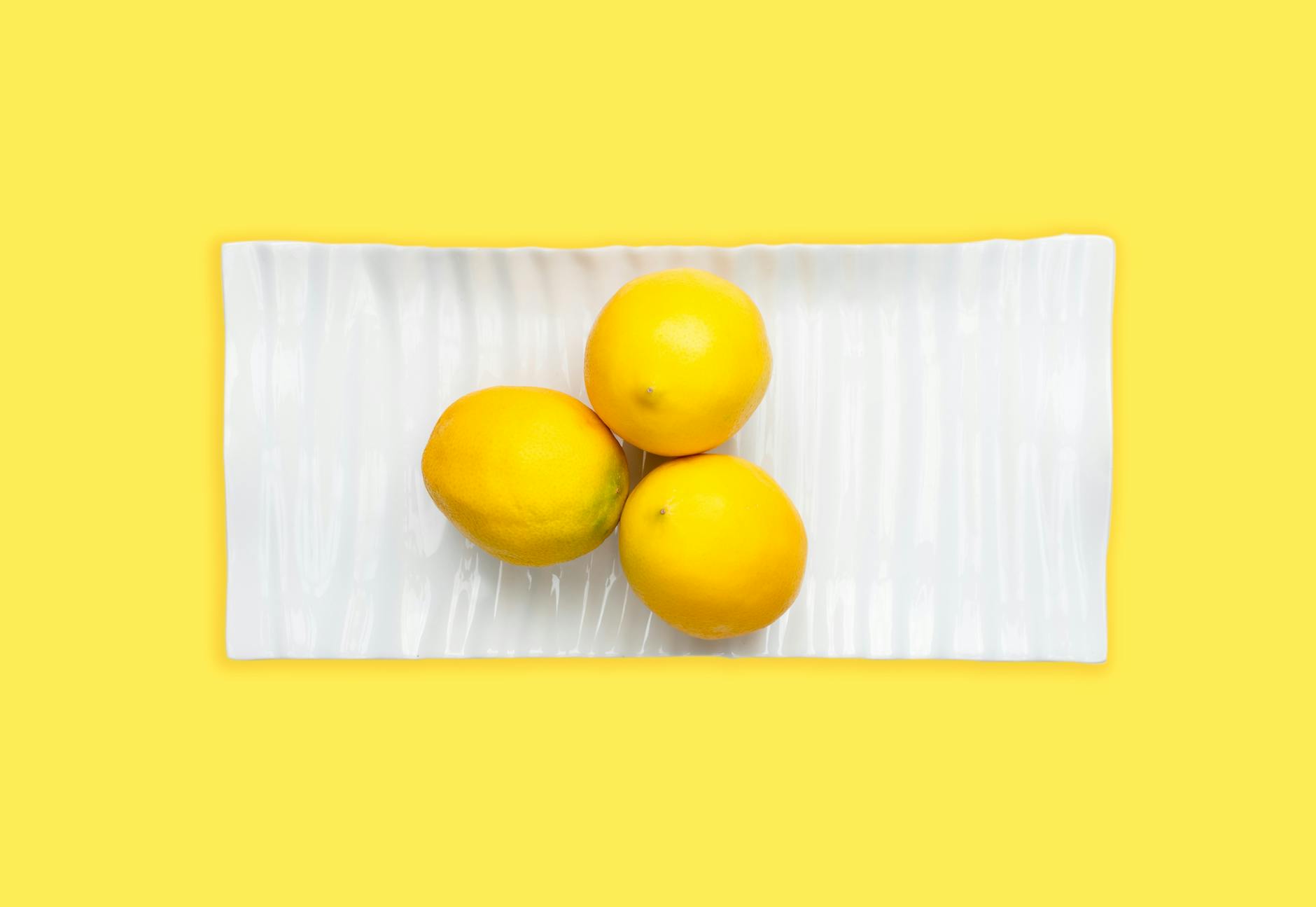 Fresh lemons arranged on a white plate with vibrant yellow background