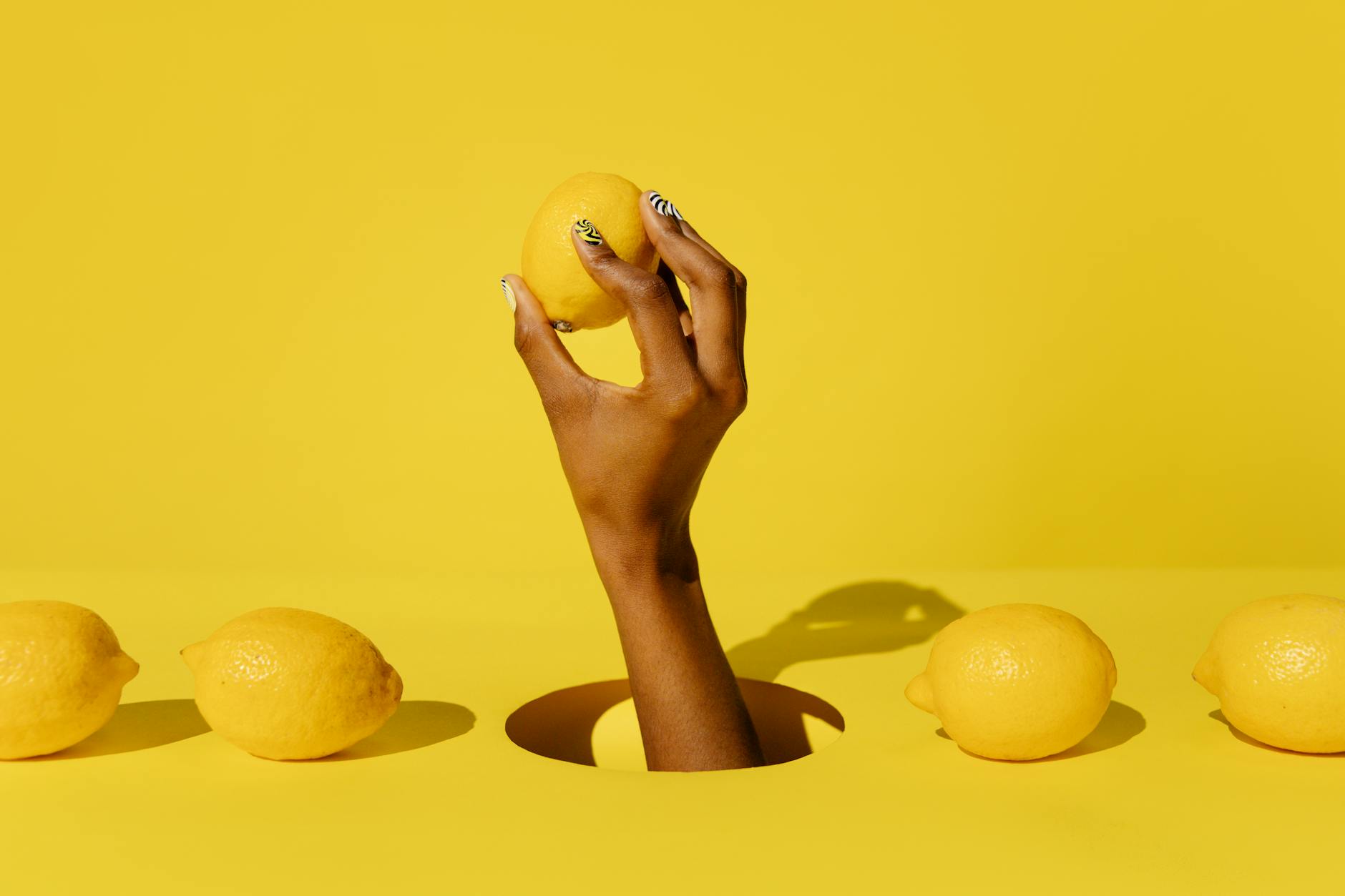 A hand holding a fresh yellow lemon against a bright yellow background