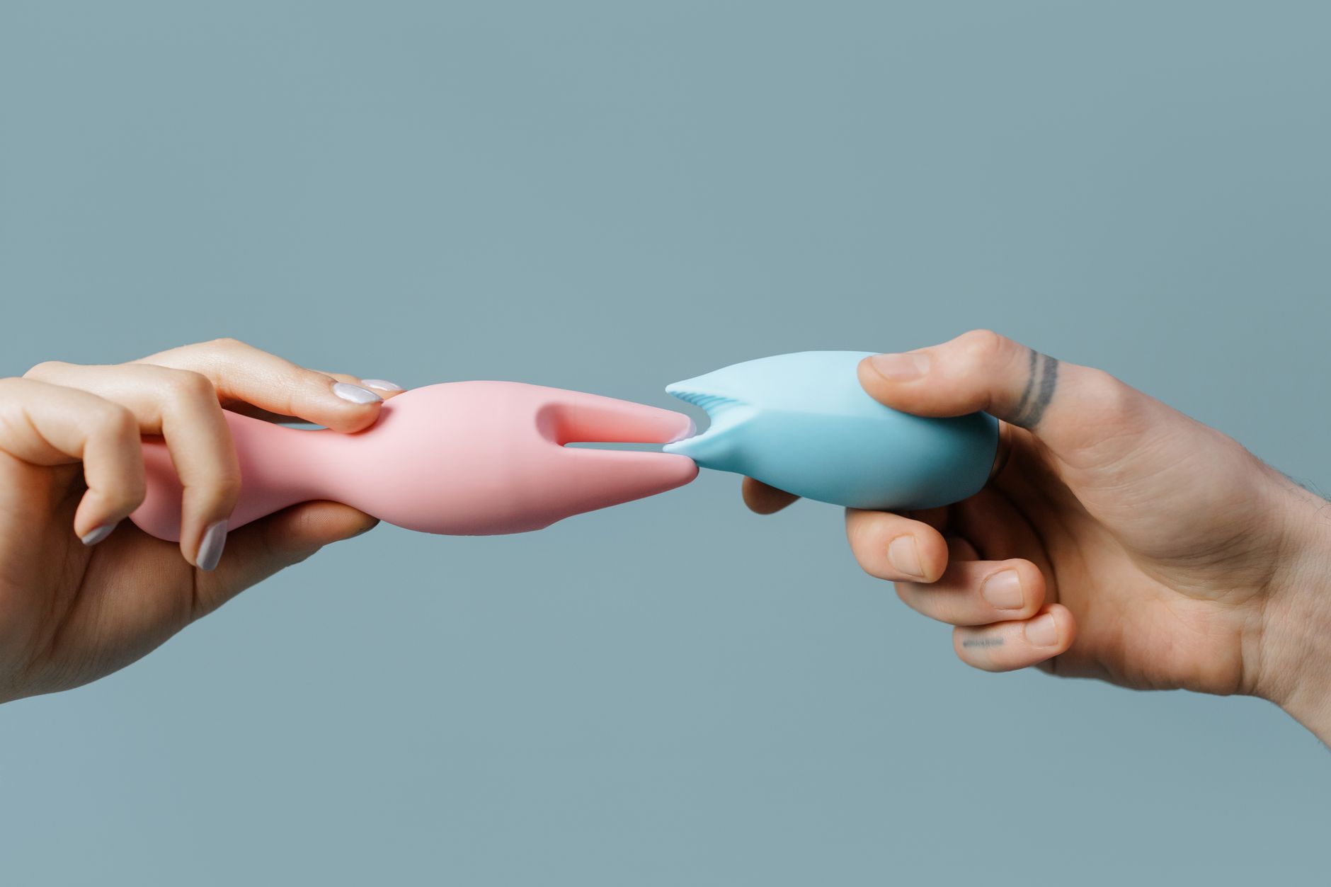 Hands holding pastel-colored silicone toys for intimate wellness