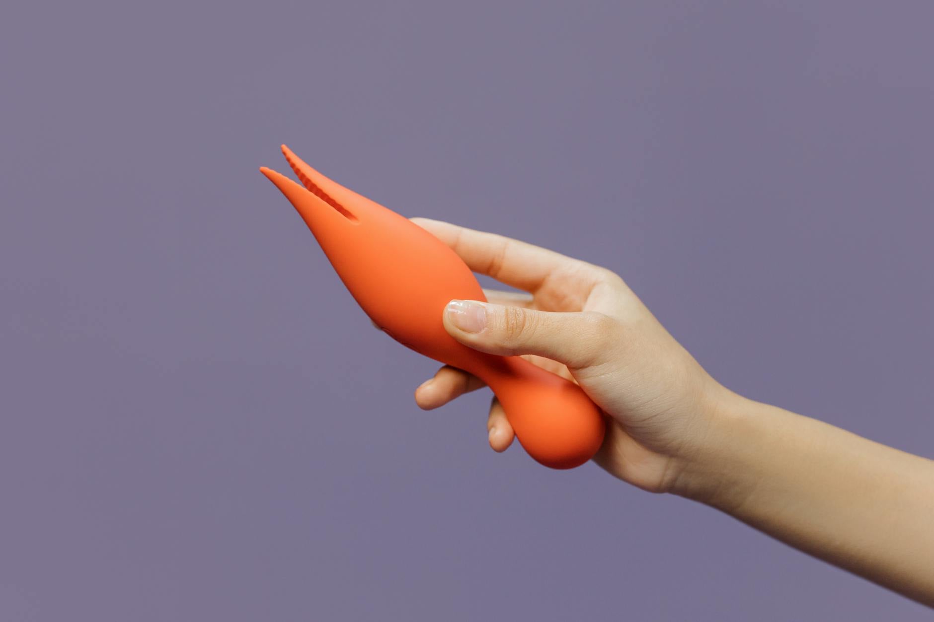 A hand holding a soft silicone lemon vibrator against a purple background