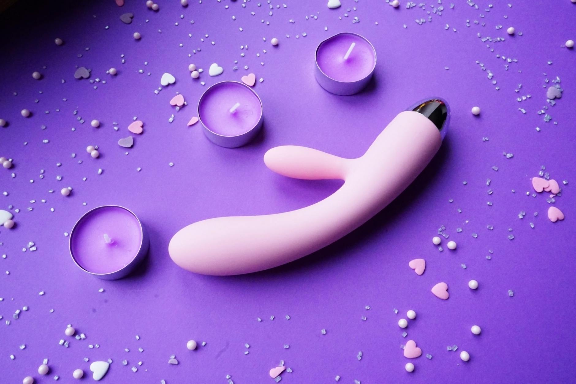 A pink lemon vibrator on purple background with romantic candles and confetti, symbolizing intimacy and pleasure